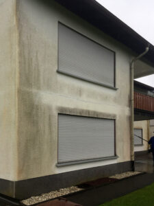 Hausfassade mit dunklen und braunen Flecken sowie Feuchtigkeitsrändern unter Fensterbänken.